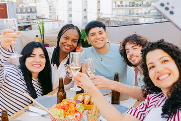 Young Latin friends gathering on a outdoor terrace, smiling while taking a selfie with a phone