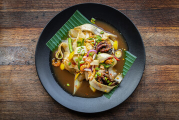 Thai Food photography of Thai or Laos style called Som Tum spicy papaya salad aka Tum Luang Prabang on banana leaf with wooden table background