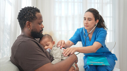 Fototapeta premium A doctor uses a stethoscope to check on the health of a little boy as he sleeps in his father's arms