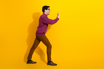 Side view of a young man gesturing with his hands, wearing stylish casual clothing, standing against a vibrant yellow background
