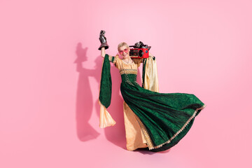 Young woman in medieval-themed dress with modern flair holding a boombox against pink background
