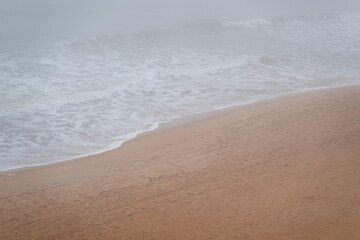 Coastal landscape with gentle waves and sandy shore during foggy weather creating a serene atmosphere in the early morning hours