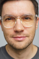 Close-up of a man with glasses displaying a calm expression in a neutral background