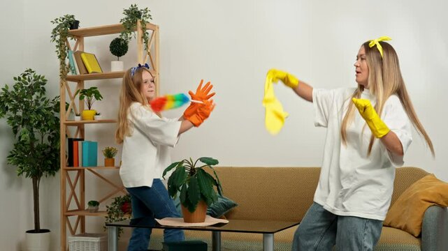 Mother and daughter cleaning the room, wiping dust with brush dancing singing and having fun. Mom teaching little girl how to keep the house clean. Slow motion.