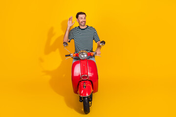 Naklejka premium Young bearded man riding bright red scooter on vibrant yellow background waving with a cheerful and stylish expression
