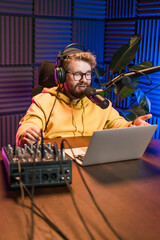 Cheerful young man recording podcast in studio. Confident man with headphones and microphone...