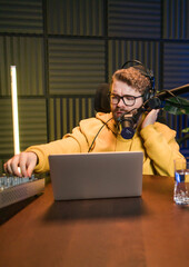 Cheerful young man recording podcast in studio. Confident man with headphones and microphone...