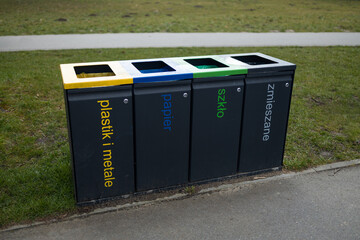 Four separate trash bins for recycling in the park, each labeled for plastic, paper, metal, and...