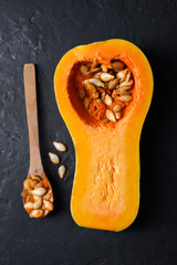 Top view of raw butternut squash with wooden spoon and seeds on black table. Half of pumpkin close up. Food photography
