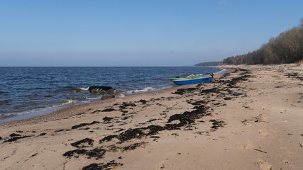 Rustic Fishing Boats Resting on the Beach Surrounded by Seaweed and Driftwood. 21.03.2025. Liepupe. Latvia.