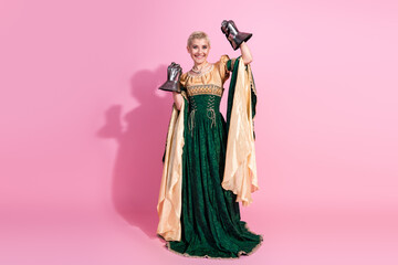 Fototapeta premium Young woman in medieval royal attire holding decorative items against a pink backdrop