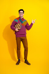 Smiling young man in trendy casual attire holding a chessboard and pointing against a vibrant vertical yellow background.
