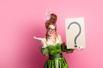 Elegant woman in baroque-style green gown posing with question sign against pink wall