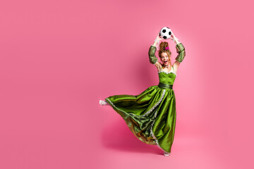 Elegant woman in baroque style green dress playing with a soccer ball on pink background