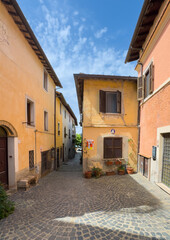 Trevignano Romano, Lazio, Italy - July 7, 2024: Via Dogali, looking from Via Umberto to the Lake shoreline under blue cloudscape. Yellow and rose facades. Some potter plants