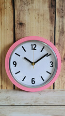 Pink wall clock showing time on wooden background, perfect for home decor or time management concepts