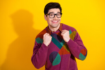 Smiling young man in vibrant geometric sweater and glasses celebrating against a bright yellow...
