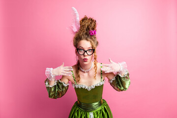 Young Woman in Green Historical Gown Posing Against Pink Backdrop with Playful Expression