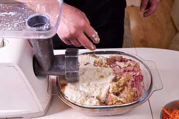 a man chops meat and vegetables in an electric meat grinder to make mincemeat for cutlets