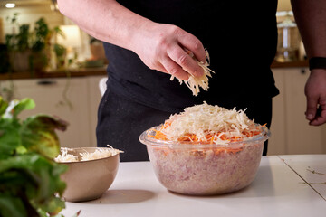 A man mixes dietary minced chicken and vegetables in a glass bowl with his hands