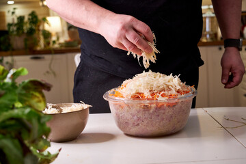 A man mixes dietary minced chicken and vegetables in a glass bowl with his hands