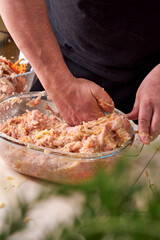 A man mixes dietary minced chicken and vegetables in a glass bowl with his hands
