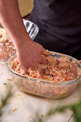 A man mixes dietary minced chicken and vegetables in a glass bowl with his hands