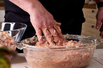 A man mixes dietary minced chicken and vegetables in a glass bowl with his hands