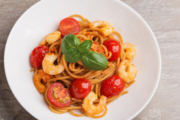 Top view on whole grain spaghetti pasta with shrimp, cherry tomato in a white bowl on stone background. Mediterranean cuisine.