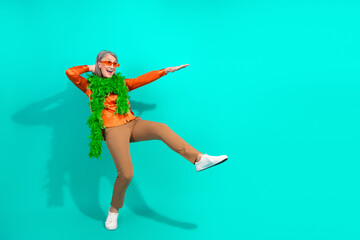 Stylish elderly woman in elegant clothing striking a playful pose against a vibrant teal background