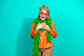 Stylish Elderly Woman in Orange Blouse and Green Boa Posing with Enthusiasm Against Turquoise Background