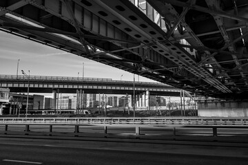 The highway under the railway bridge in Moscow against the background of the city and the car park. Black and white photo.