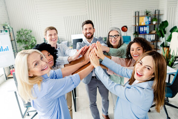 Group of colleagues in formalwear joining hands in a gesture of teamwork and unity at a modern corporate office