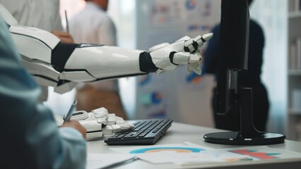 A robotic arm interacts with a computer in a contemporary office, highlighting the synergy between technology and teamwork in business innovation and analysis.Noogenesis