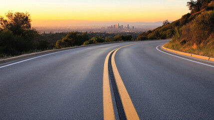 Fototapeta premium A winding road stretches through green hills, leading down to a vibrant city skyline. The sun sets behind the city, casting a warm glow over the landscape and the horizon