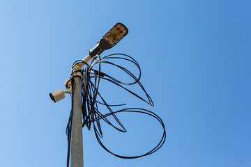 Street lamp with tangled cables and security camera against clear blue sky, concept of urban...