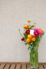 Bouquet of colorful Ranunculus in the transparent glass vase on the wooden table, with copy space
