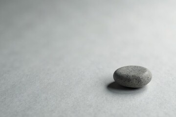 A small stone or pebble on the surface of light gray kraft paper, nature, element, minimalist