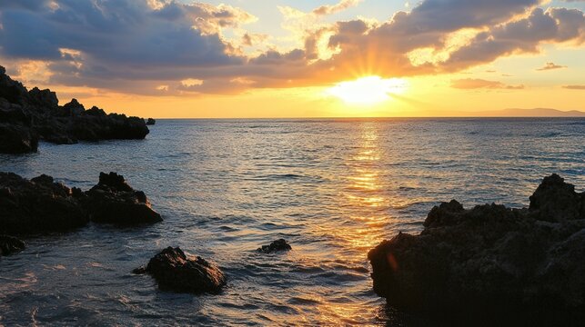 Golden sunset over tranquil ocean with rocky shoreline and dramatic clouds