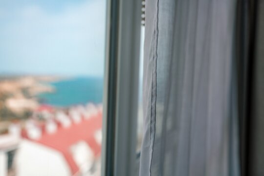 Fototapeta Window View Blinds: Coastal town seen through hotel window during daytime for relaxation.