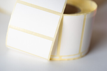 Close-up of a curled roll of blank self-adhesive labels with a yellow border, commonly used for...