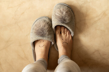 Drawing 2025 with sadness and on the second leg a smile is drawn on the legs of a girl in slippers with pompoms on the floor of the house, difficulties