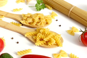 On a white background lie two wooden spoons with pasta.