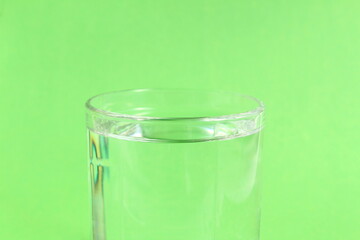 On a green background there is a glass cup with transparent clean drinking water.