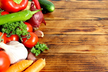 Background of different fresh vegetables lying on a wooden table with space for text.