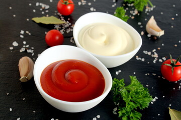 Two types of sauce mayonnaise and ketchup in bowls stand on a black background.