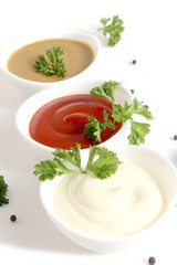 Three types of sauces in bowls stand on a white background.