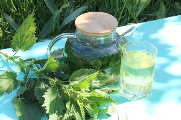 A decoction of nettle leaves in a teapot stands on a wooden table.