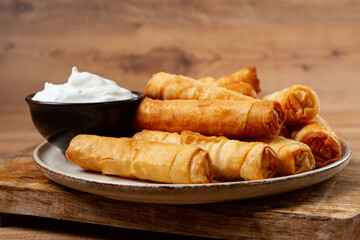 fried spring rolls with cheese, on a wooden background, with cream sauce, no people,