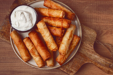 fried spring rolls with cheese, on a wooden background, with cream sauce, no people,